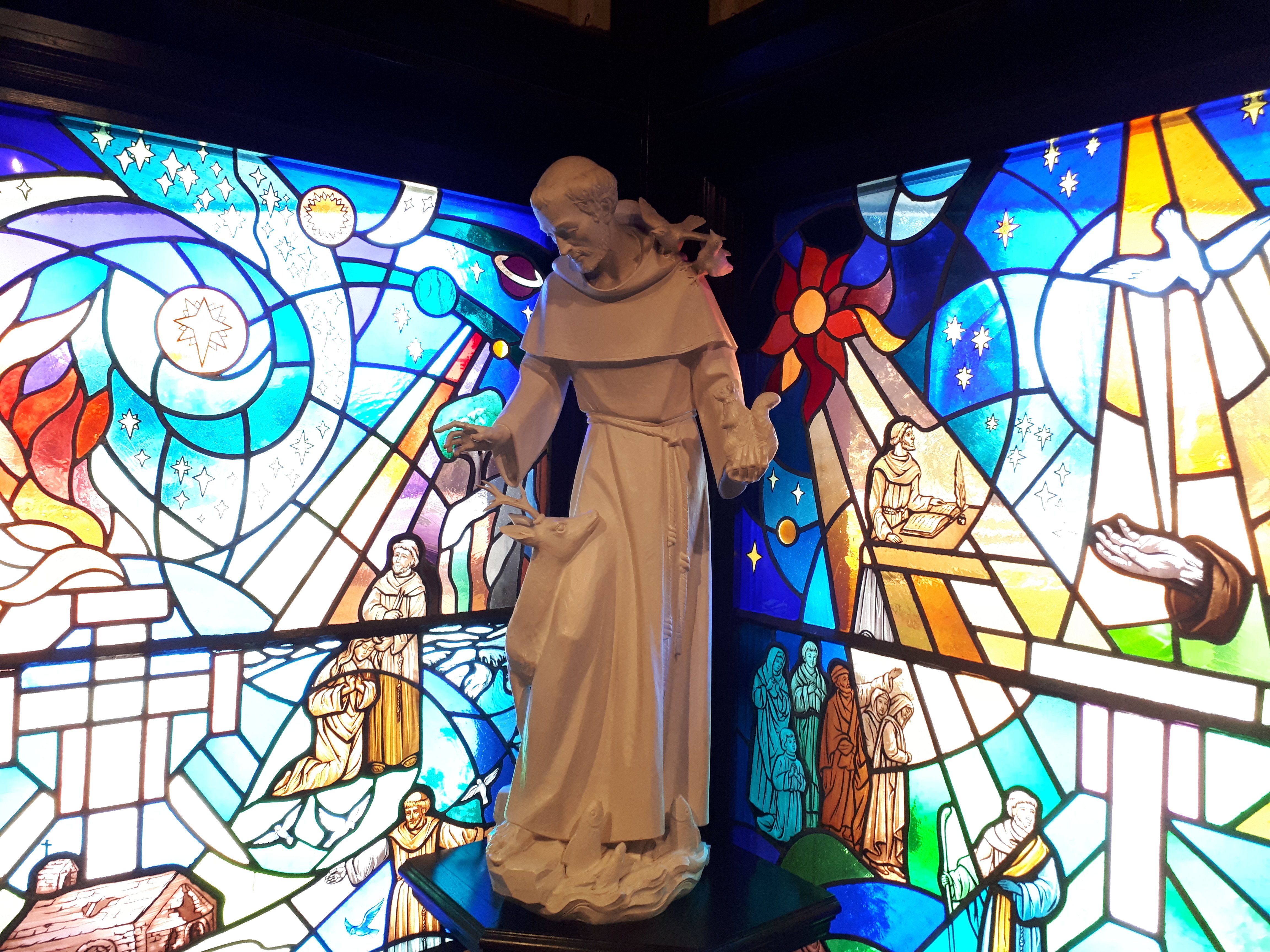 St. Francis Standing infront of Stain Glass Windows
